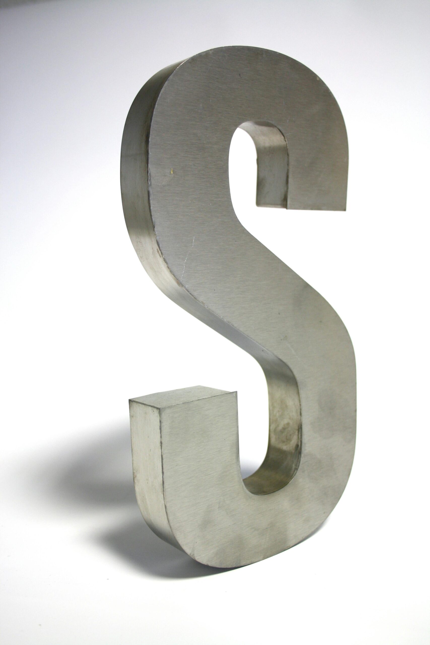 Close-up of a metallic letter S sculpture made of silver iron on a white background.